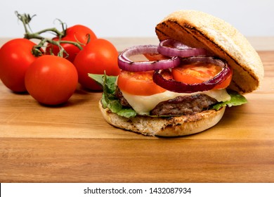 Cheeseburger With Havarti Cheese Tomatoes And Red Onions And Lettuce On A Toasted Cornmeal Bun On A Wooden Table With Bun Open Showing Ingredients
