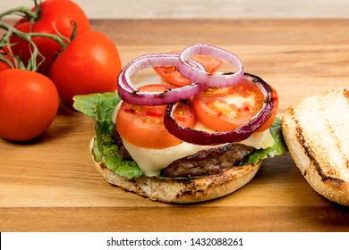 Cheeseburger With Havarti Cheese Tomatoes And Red Onions And Lettuce On A Toasted Cornmeal Bun On A Wooden Table With Bun Open Showing Ingredients