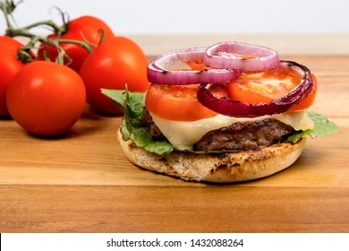 Cheeseburger With Havarti Cheese Tomatoes And Red Onions And Lettuce On A Toasted Cornmeal Bun On A Wooden Table With Bun Open Showing Ingredients