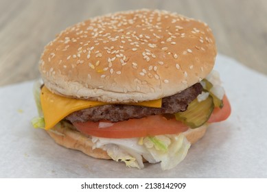 Cheeseburger Sandwich Loaded With Sliced Tomatoes, Pickles, And Lettuce On Top Of A Sesame Seed Bun.