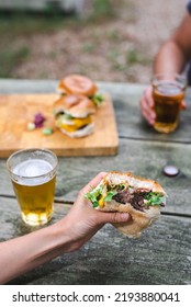 Cheeseburger In An Unrecognizable Female Hand Next To A Glass Of Beer. Suburban Lifestyle.