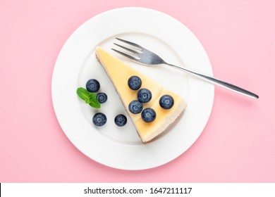 Cheesecake with blueberries on pink background. Top view. Girl's dessert. Classical plain New York cheesecake on white plate