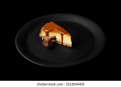 Cheesecake With Caramel And A Chocolate Nail Stuck Inside In A Plate On A Black Background