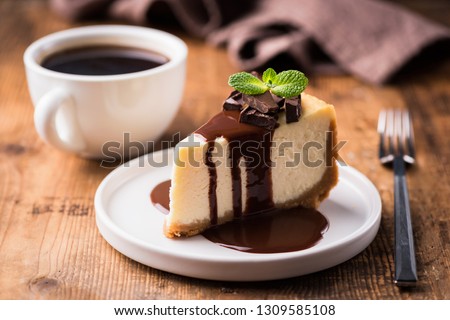 Cheesecake with chocolate sauce and cup of black coffee on a wooden table. Tasty snack or coffee time with slice of cake