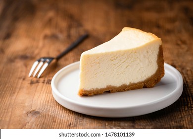 Cheesecake slice, New York style classical cheese cake on wooden background. Slice of tasty cake on white plate served with dessert fork