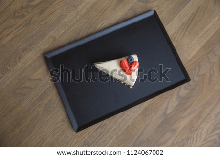 Cheesecake with strawberries and blueberries. In black rectangular dishes. On a wooden table is brown.