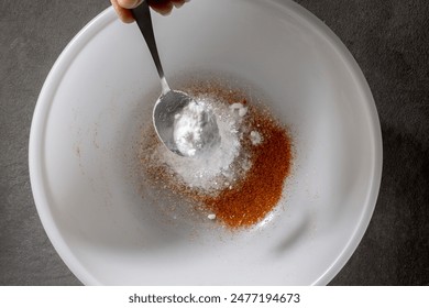 chef add baking powder into a white bowl with a metal spoon, prepares mix of spices for chicken wings. process of making crispy chicken wings