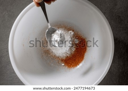 chef add baking powder into a white bowl with a metal spoon, prepares mix of spices for chicken wings. process of making crispy chicken wings