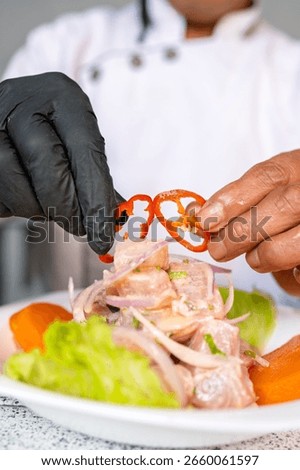 Chef adding final touch to a plate of peruvian ceviche, using slices of red pepper to enhance flavor and presentation