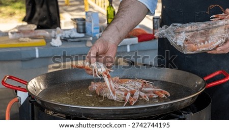 Chef adding fresh langoustines to large frying pan at outdoor food festival