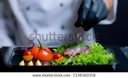 Chef is adding salt to the dish in slow motion. Chef is out of focus on the background