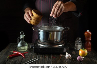 The chef adds salt to the pot of hot food. Cooking a diet lunch in the kitchen of a hotel or restaurant. - Powered by Shutterstock