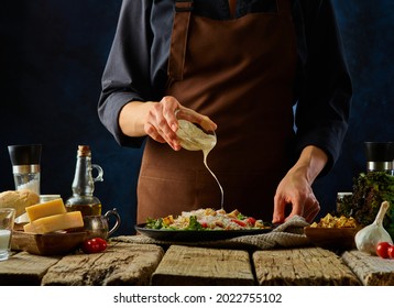 The chef adds the sauce to the Caesar salad. The ingredients for the salad are on the table. Dark blue background. Lots of ingredients. Restaurant, hotel, home cooking. A festive dish. - Powered by Shutterstock