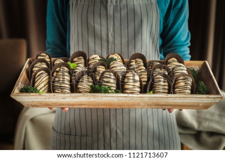 Chef in apron holding wooden tray with delicious profiteroles with chocolate glaze