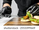 A chef in black gloves assembles a delicious bao bun filled with fresh vegetables and meat. The vibrant colors of the ingredients create an appealing and appetizing dish on a wooden board.