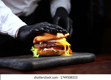 Chef in black gloves cooking a hamburger. Horizontal photo. An unrecognizable photo on a black background. Copy of the space - Shutterstock ID 1749508313