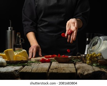 A Chef In A Black Uniform Is Cutting Tomatoes On A Cutting Board. Levitation. Ingredients For Making Salad, Pizza, Sauce, Pie. Wood Texture. Cookbook, Culinary Blog, Instagram.
