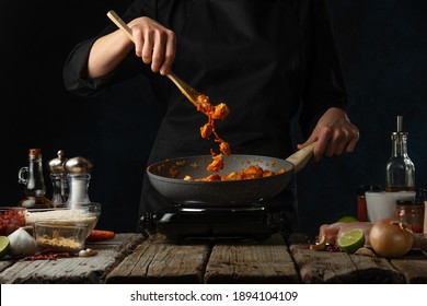 Chef in black uniform mix frying chicken fillet with sauce. Backstage of cooking traditional Indian chicken curry on dark blue background. Concept cooking process. Hot recipe. Frozen motion. - Powered by Shutterstock