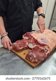 Chef breaking down large raw beef primal cut on wooden board — butchery technique, professional kitchen