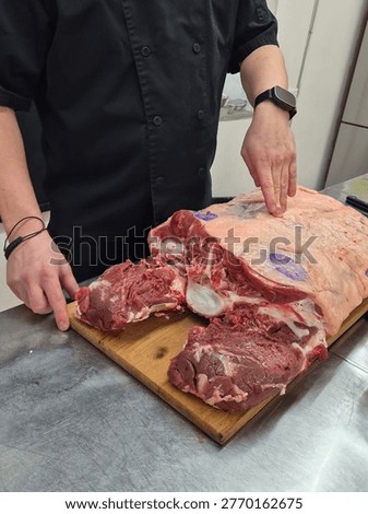 Chef breaking down large raw beef primal cut on wooden board — butchery technique, professional kitchen