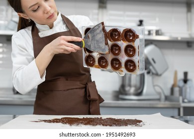 Chef or chocolatier makes sweet chocolates in a professional kitchen. She turns the mold over and pours the rest of the chocolate onto the table