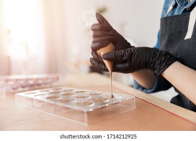 Chef Or Chocolatier Pouring Melted Dark Chocolate Into Silicone Molds On Pastry Bag.