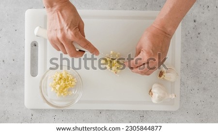 The chef chopping garlic on a white plastic cutting board, close-up view, preparation process, recipe