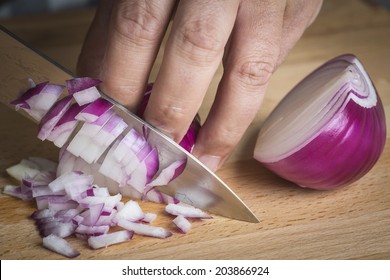 Chef chopping a red onion with a knife on the cutting board