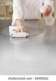 A Chef Is Cleaning A Counter In A Professional Kitchen With A Bottle Of Solution And A Rag.  Vertically Framed Shot.