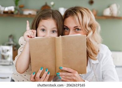 Chef cook baker mom woman in white shirt work baby girl helper read cookbook point finger up hide at kitchen table home Cooking food process concept Mommy little kid daughter prepare fruit sweet cake - Powered by Shutterstock