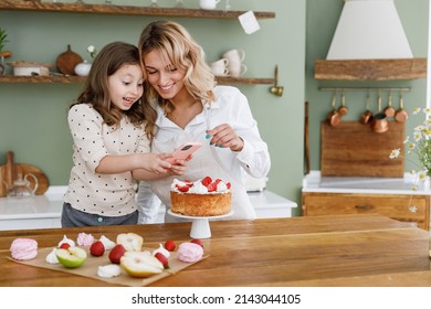 Chef cook baker mom woman in white shirt work with amazed baby girl helper take picture on mobile cell phone at kitchen table home. Cooking food process concept Mommy little kid daughter prepare cake. - Powered by Shutterstock