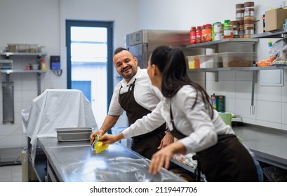 Chef And Cook Cleaning The Workspace After Doing Dishes Indoors In Restaurant Kitchen.