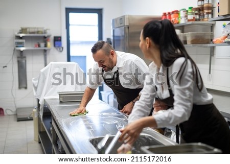 Chef and cook cleaning the workspace after doing dishes indoors in restaurant kitchen.