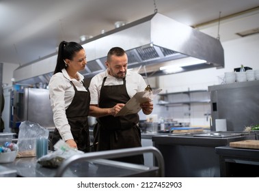 Chef and cook discussing menu indoors in restaurant kitchen. - Powered by Shutterstock