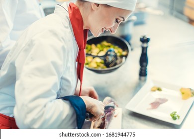 Chef Cook In Fancy Restaurant Kitchen Slicing Ham For A Dish With Plate Of Food In The Background