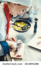 Chef Cook In Fancy Restaurant Kitchen Slicing Ham For A Dish With Plate Of Food In The Background