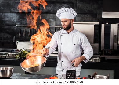 Chef cook food with fire at kitchen restaurant. Cook with wok at kitchen. Chef male in uniform hold wok with fire. - Shutterstock ID 1758967079