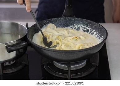 Chef cook hand making handmade tortellini ravioli with cream sauce wok pan on stove fire. - Powered by Shutterstock