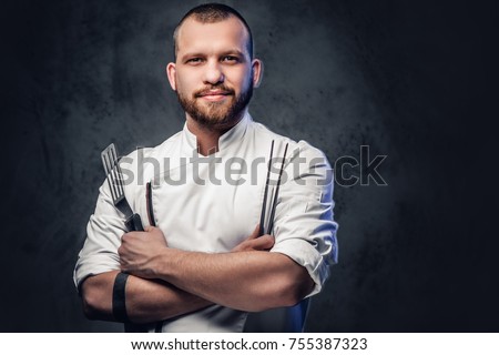 Chef cook holds a knife over dark grey background.