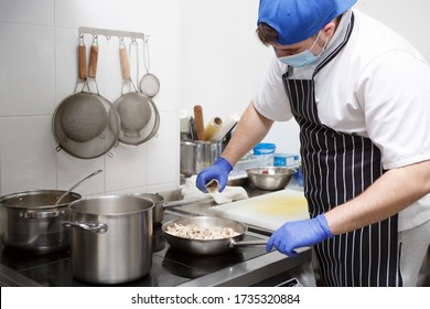 Chef Cook. Man In Mask And Gloves Adding Spices To Fresh Mushrooms On Frying Pan, Safe Culinary