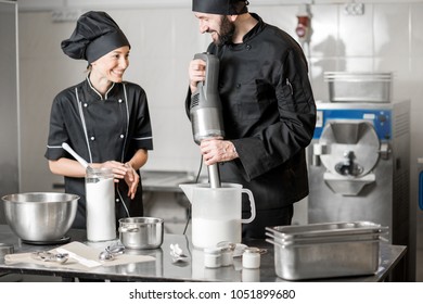 Chef Cook With Young Woman Assistant Making Ice Cream Together Mixing Ingredients In The Professional Kitchen Of The Small Manufacturing