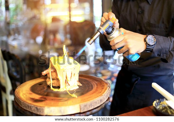 Chef cooking of Crispy Fried Chicken Lava Cheese on\
wooden board background in the restaurants, with the man hand\
spraying the blow torch into the hot cheese. Foods concept. Warm\
lights tone.