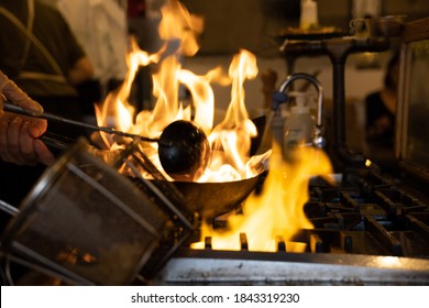 Chef Cooking Curry In A Wok In A Black Iron Pan Over Blazing Flames.