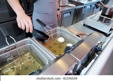 Chef Cooking Dish In A Deep Fryer In Boiling Oil On Restaurant Kitchen