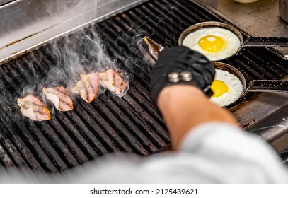 Chef Cooking  Eggs And Bacon In Pan On Grill In Kitchen