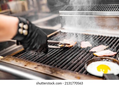 Chef Cooking Eggs And Bacon In Pan On Grill In Kitchen