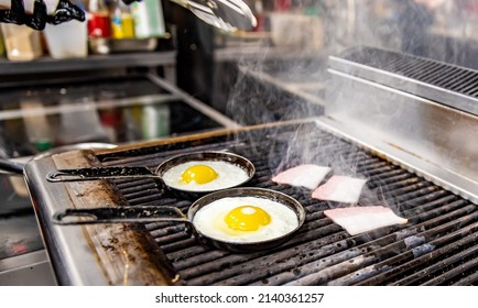 Chef Cooking Eggs And Bacon In Pan On Grill In Kitchen