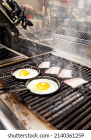 Chef Cooking Eggs And Bacon In Pan On Grill In Kitchen