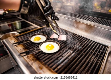 Chef Cooking Eggs And Bacon In Pan On Grill In Kitchen