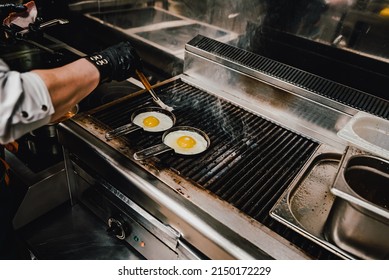 Chef Cooking Eggs In Pan On Grill In Kitchen